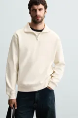 Sudadera color crema de corte recto, con cuello polo y cierre de cremallera metálica.