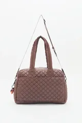 Bolso marrón con diseño matelassé, doble asa corta, correa larga desmontable y dos bolsillos frontales. Incluye llavero de corazón y dijes desmontables.