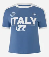 Remera de algodón celeste con cuello redondo y mangas cortas con ribete blanco. Estampado frontal con la palabra "Italy" y otros motivos gráficos en blanco.