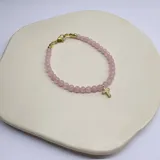 Pulsera elástica con cuentas de cuarzo rosa y dije de cruz dorada con incrustaciones brillantes.