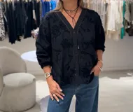 Camisa negra de manga larga con puños elásticos, cierre frontal con botones y apliques bordados de flores en la parte delantera y trasera.