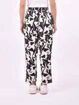 Pantalón babucha de tela estampada con hojas en tonos rosa, naranja y azul, con cintura elastizada y lazo para ajustar.