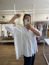 Camisa de algodón color amarillo con diseño de línea italiana, corte holgado y asimétrico. Presenta cuello camisero, cierre frontal con botones y detalle de pliegues verticales en el pecho. Cuenta con mangas largas y puños con botón.