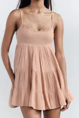 Vestido corto color salmón, de escote recto y tirantes finos ajustables. Presenta detalle de encaje en el escote y falda de tres niveles.