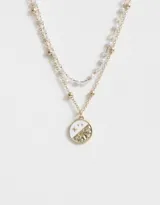 Collar corto dorado de doble cadena, una con cuentas pequeñas y otra con bolitas. Dije redondo esmaltado en blanco con diseño de sol y estrellas.