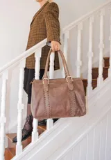 Bolso marrón de cuero con doble asa corta y cierre superior con cremallera. Tiene detalles de costuras a los lados y aplique con el nombre de la marca.