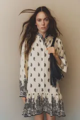 Vestido corto de viscosa color crema con estampado paisley en negro, cuello mao, botones frontales, mangas largas abullonadas con puños abotonados y falda con volantes.