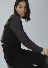 Chaleco negro corto con cuello redondo y cierre frontal con botones.