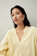 Blusa color amarillo pálido de manga larga con escote en V, mangas abullonadas con volados y botones forrados.