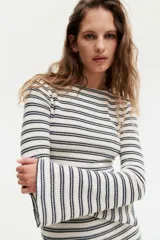 Vestido largo de punto texturizado a rayas horizontales en blanco y negro. Tiene cuello redondo, mangas largas y tajo lateral pronunciado.