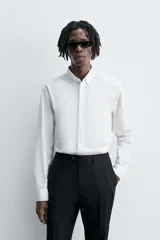 Camisa de algodón color celeste claro, corte regular fit, con cuello abotonado (button-down), manga larga con puño abotonado y bolsillo de parche en el pecho izquierdo.