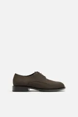 Zapato de vestir tipo derby color marrón oscuro, con capellada de cuero serraje, horma redonda, cordones finos al tono y suela con ligero tacón.