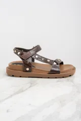 Sandalias marrones de cuero con suela gruesa y tachas doradas en forma de estrella y circulares.