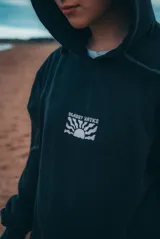 Buzo hoodie negro con efecto lavado y estampado blanco en el pecho con la frase "Glassy Waves" y un diseño de sol y olas.