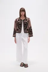 Chaqueta corta de algodón color marrón topo, sin cuello, con bordados florales y de estilo paisley en negro. Presenta un borde festoneado y mangas largas.