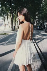 Minivestido blanco con cuello halter ajustable con lazos y falda escalonada con volantes. Espalda descubierta.