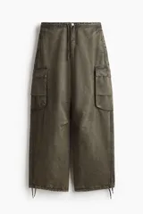 Pantalón cargo verde oliva de corte amplio, con cintura elástica ajustable con cordón, bolsillos laterales, bolsillos traseros con solapa y botón a presión, bolsillos cargo con solapa en las piernas, pliegues en la rodilla y cordón ajustable en el bajo.