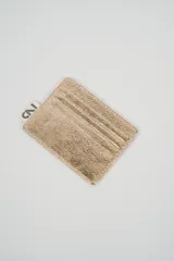 Tarjetero metálico color plateado con textura rugosa y costuras visibles. Incluye una pequeña etiqueta de marca en la parte superior.