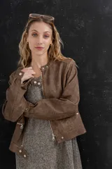 Chaqueta tipo biker de cuero ecológico (PU) color marrón oscuro con efecto desgastado. Presenta cuello mao con broches metálicos, cierre frontal y bolsillos con cremallera.