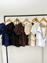 Blusa azul marino de algodón italiano, con escote elastizado que permite usarla con los hombros al descubierto o como remera con hombro abullonado. Presenta volados y mangas cortas abullonadas.