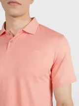 Chomba de piqué color salmón, de corte clásico, con cuello polo y tapeta de dos botones.