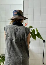 Vestido corto de jean gris con botones frontales, sin mangas, con cuello camisero y bolsillos en el pecho.