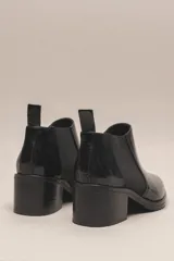 Botín negro de cuero vacuno con acabado charol, estilo botín Chelsea con puntera fina y elástico lateral. Posee un taco ancho y bajo de 5.5 cm.