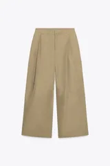 Pantalón color beige de tiro medio con trabillas, bolsillos laterales, de plastrón en pierna y detalle de solapas en espalda. Detalle de pinzas en delantero y cierre frontal con cremallera y ganchos metálicos.