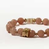 Pulsera elástica con cuentas facetadas color durazno, separadores de metal dorado, cuenta de nácar y dije circular dorado.