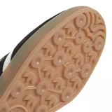 Zapatillas Adidas Gazelle Indoor negras con las tres tiras laterales blancas, detalle dorado con el nombre del modelo y suela de goma color caramelo.