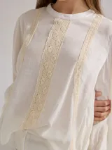 Camisa blanca de lino y viscosa, de corte holgado, con cuello redondo y mangas largas abullonadas. Presenta detalles de puntilla de algodón en el frente.