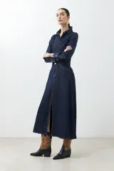 Vestido camisero de jean azul oscuro, corte evasé, largo midi, con cuello camisero, cierre frontal con botones, mangas largas con puños abotonados, bolsillos en el pecho y tajo lateral.