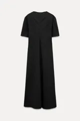 Vestido midi negro de cuello redondo y manga corta, con bolsillos laterales ocultos y costuras marcadas. Tiene corte evasé con abertura en la espalda y cierre trasero con cremallera oculta.