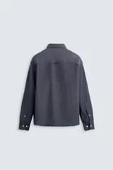 Camisa azul de algodón con textura chambray, corte regular fit, cuello abotonado, manga larga con puños abotonados, bolsillo de parche en el pecho y cierre frontal con botones.