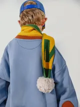 Bufanda azul y marrón con pompones grises, confeccionada en algodón.