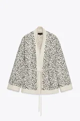 Kimono abierto color crudo con bordados florales negros y abalorios. Confeccionado en hilatura con lino y viscosa, de manga larga y cinturón ajustable con lazadas.