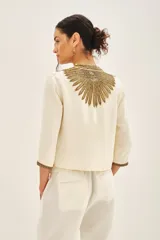 Saco corto color crema con escote en V y mangas 3/4. Confeccionado en viscosa crepe con bordado de mostacillas, canutillos y lentejuelas doradas.