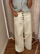 Pantalón ancho color crudo, con tiro alto, corte holgado y cierre frontal con botones.