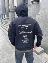 Canguro negro de algodón con capucha y cordón ajustable. Estampado en la espalda con la leyenda "EAST LONDON STUDIOS SINCE .1994", el logo de la marca Allsaints y las ciudades de París, Berlín, Nueva York y Milán.