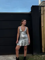 Vestido corto de lentejuelas color verde oliva, con escote en V, breteles finos cruzados en la espalda, cut-outs laterales y volado en el ruedo.