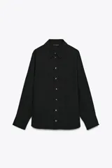 Camisa negra de satén, de corte clásico, con cuello solapa, mangas largas y cierre frontal con botones dorados.