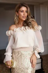 Blusa beige con escote off-shoulder con volados, mangas largas abullonadas con puños elásticos y corte ajustado.