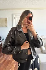 Chaqueta tipo bomber corta de cuero ovino color chocolate oscuro, forrada en su interior. Presenta detalles de pasamanería en forma de cruz en cuero marrón desgastado en ambas mangas y botones de guampa.