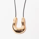 Collar con dije dorado en forma de U invertida, colgando de un cordón negro.