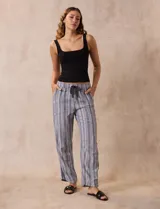 Pantalón largo de lino y rayón a rayas verticales grises y blancas. Tiene pretina elastizada con lazo de ajuste, bolsillos delanteros y traseros.