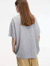Remera blanca de algodón con cuello redondo y mangas cortas, decorada con apliques de brillantes plateados de diferentes tamaños en el frente.