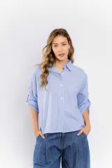 Camisa celeste a rayas verticales blancas, de corte holgado y mangas 3/4 con trabilla. Presenta cuello clásico y cierre frontal con botones.