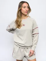 Buzo de felpa color gris claro, con cuello redondo y logo Umbro bordado en el pecho. Presenta detalles de ribete en contraste color borgoña en cuello, puños y ruedo.