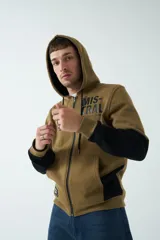 Campera marrón de felpa con capucha, cierre frontal y bolsillos laterales con cierre. Presenta mangas largas negras y logo de la marca estampado en el pecho.