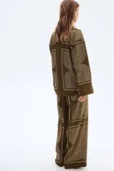 Pantalón de corte recto color marrón con estampado geométrico en blanco. Modelo de tiro alto con elástico en la parte posterior de la pretina y cierre oculto en un lateral.